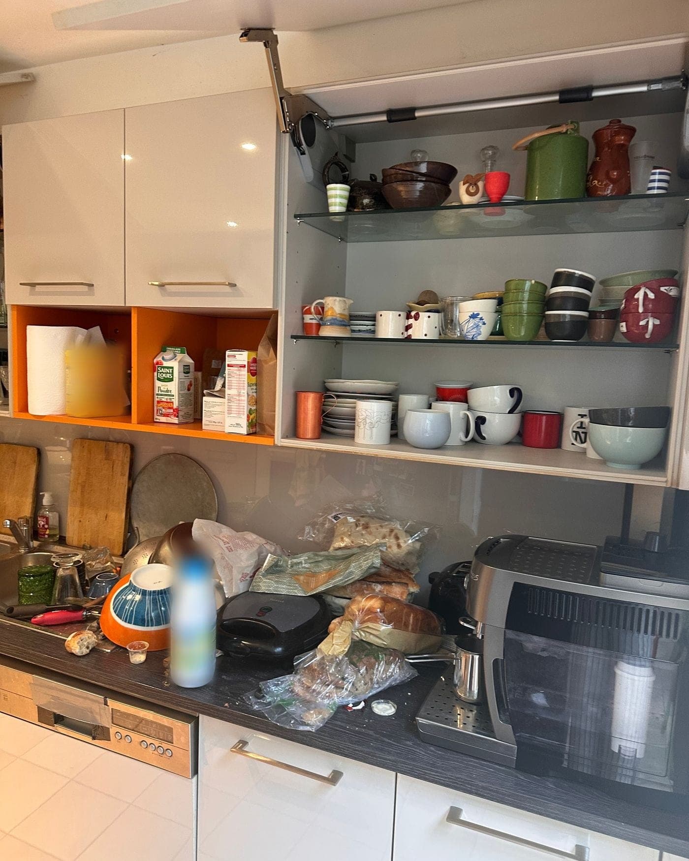 Cuisine avant le passage : placard haut relevé sur des étagères chargées, plan couvert de sachets et d'appareils