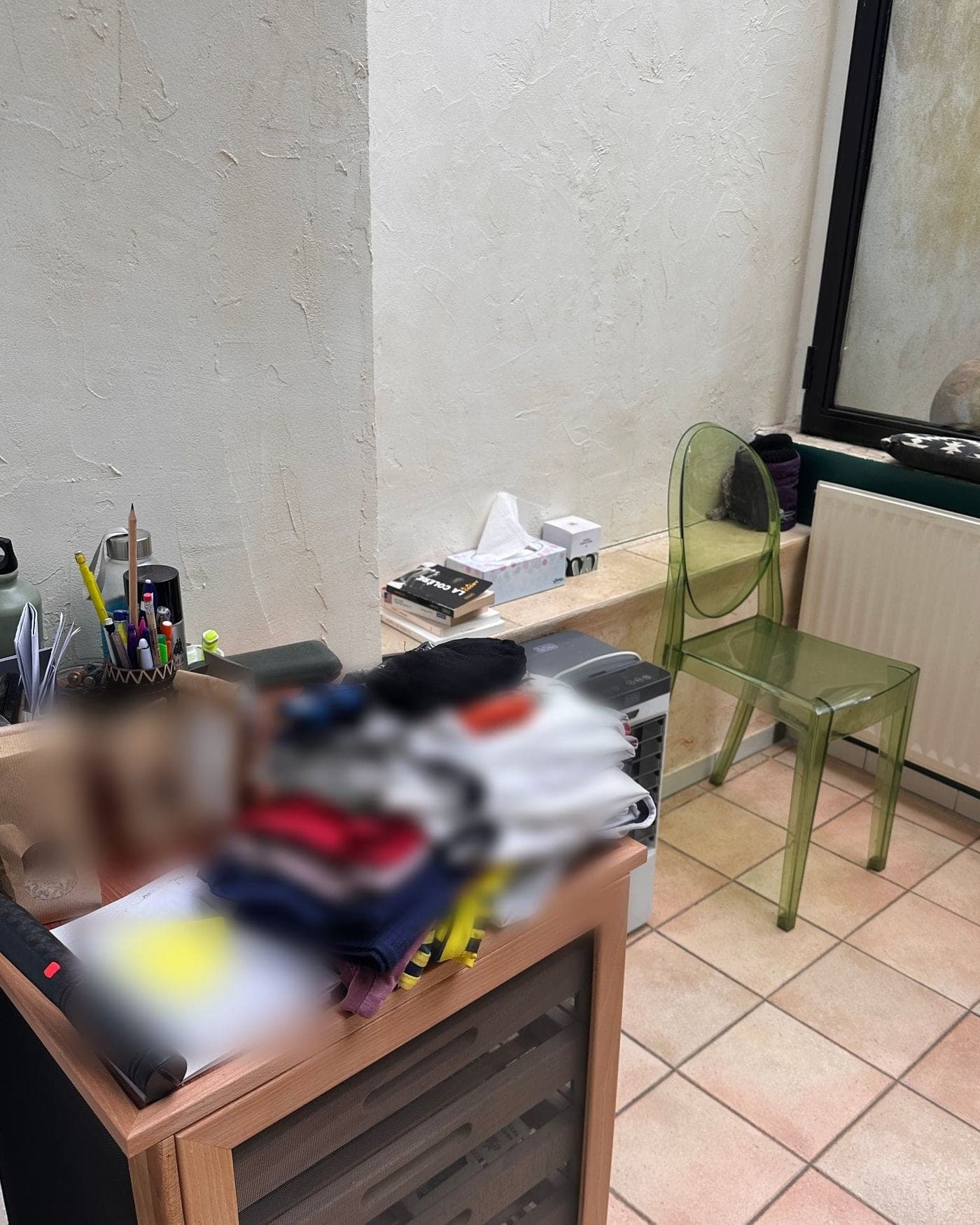 Coin de véranda avant le passage : pile de linge, sachets et cahier posés sur un meuble à tiroirs