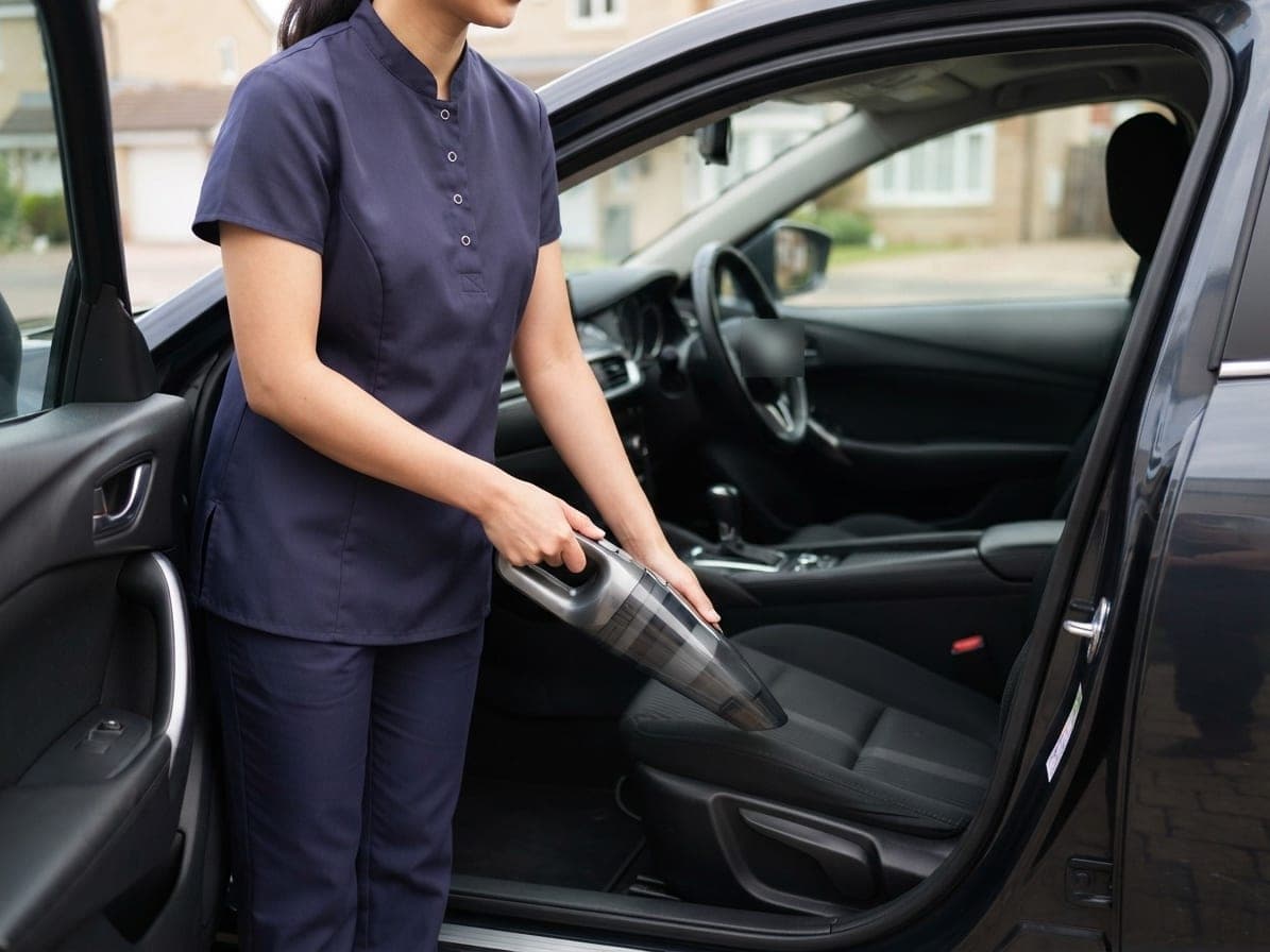 Femme en tunique bleu marine qui passe un aspirateur à main sur le siège d'une voiture, portière ouverte