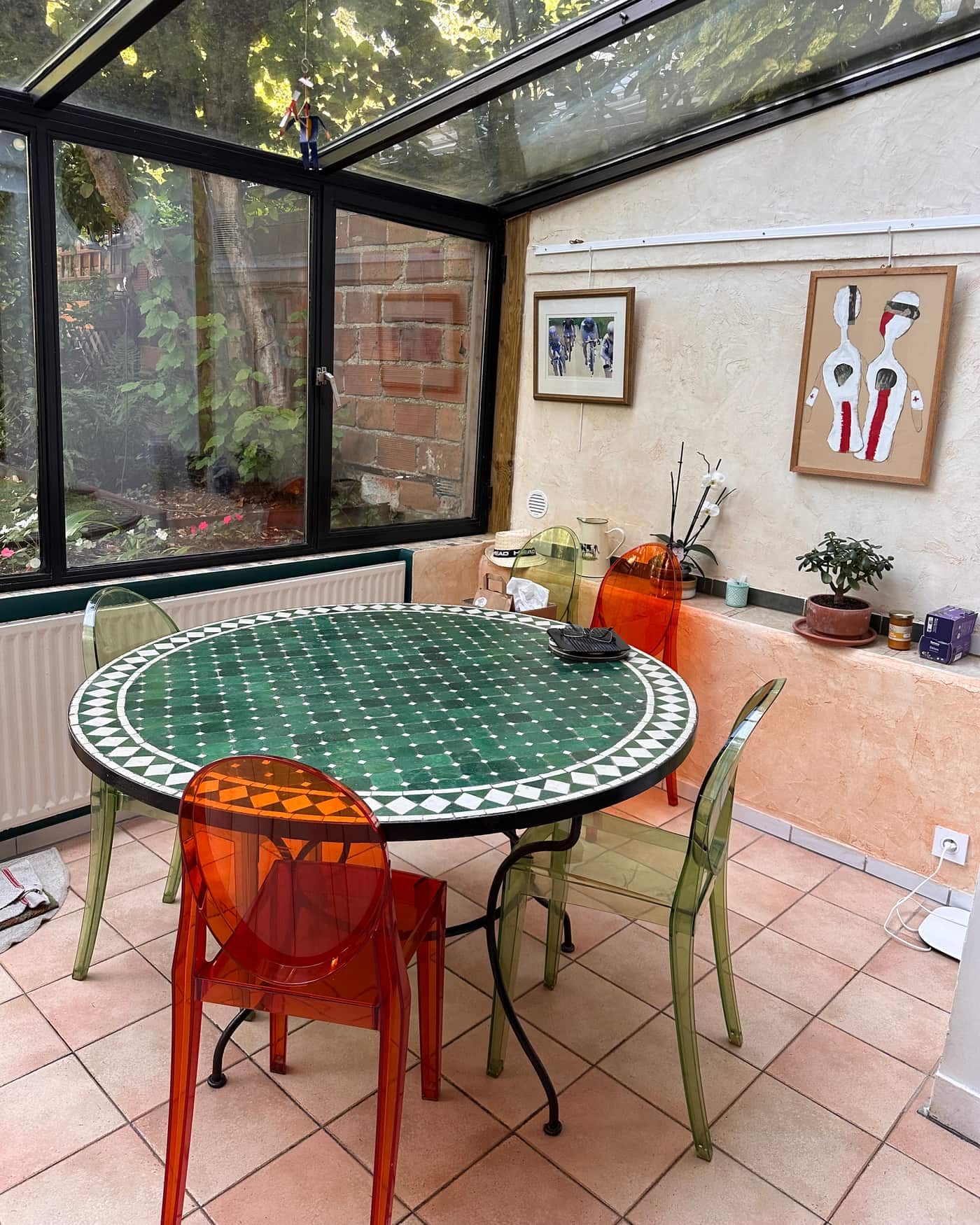 Véranda rangée : table ronde en mosaïque verte et blanche, chaises remises autour