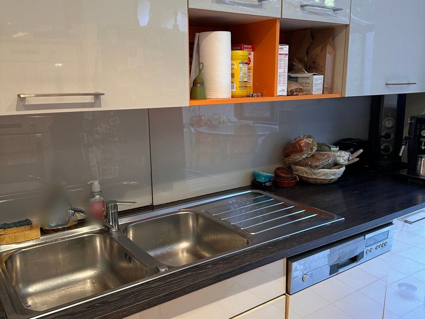 Cuisine rangée : placards blancs, niche orange, double évier et plan de travail sombre dégagé